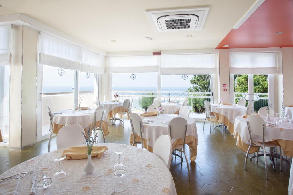 un restaurant avec des tables et des chaises blanches et des fenêtres dans l'établissement Hotel Palazzi, à Gabicce Mare