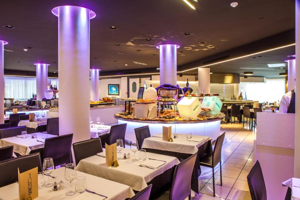 un restaurant avec des tables et des chaises blanches et un éclairage violet dans l'établissement Hotel Cesare Augustus, à Lido di Jesolo