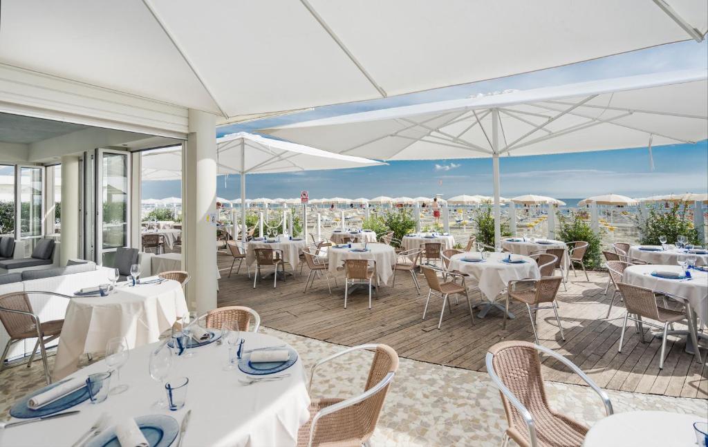 un restaurant avec des tables, des chaises et des parasols blancs dans l'établissement Hotel Le Palme - Premier Resort, à Milano Marittima