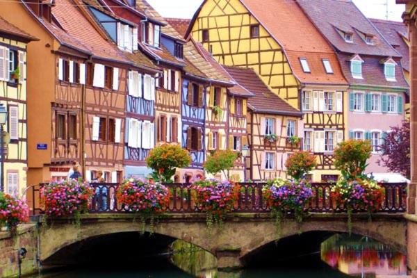 un pont sur une rivière avec des maisons et des fleurs dans l'établissement Camping du RIED, à Boofzheim
