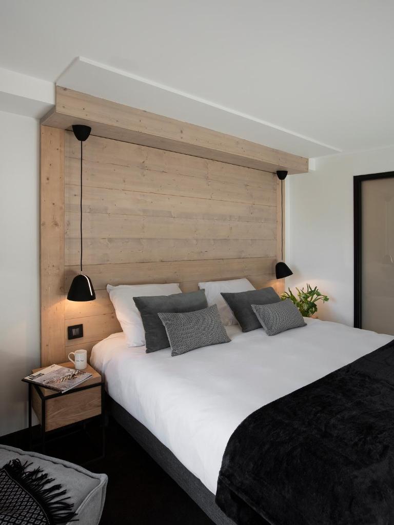 - une chambre avec un grand lit blanc et une tête de lit en bois dans l'établissement Grand Hôtel & Spa NUXE Serre Chevalier, à Saint-Chaffrey