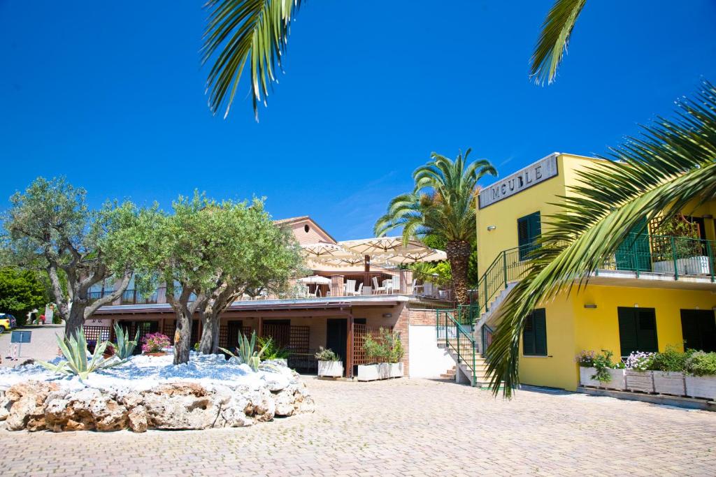 un bâtiment jaune avec un palmier devant lui dans l'établissement Hotel Le Cave, à Sirolo