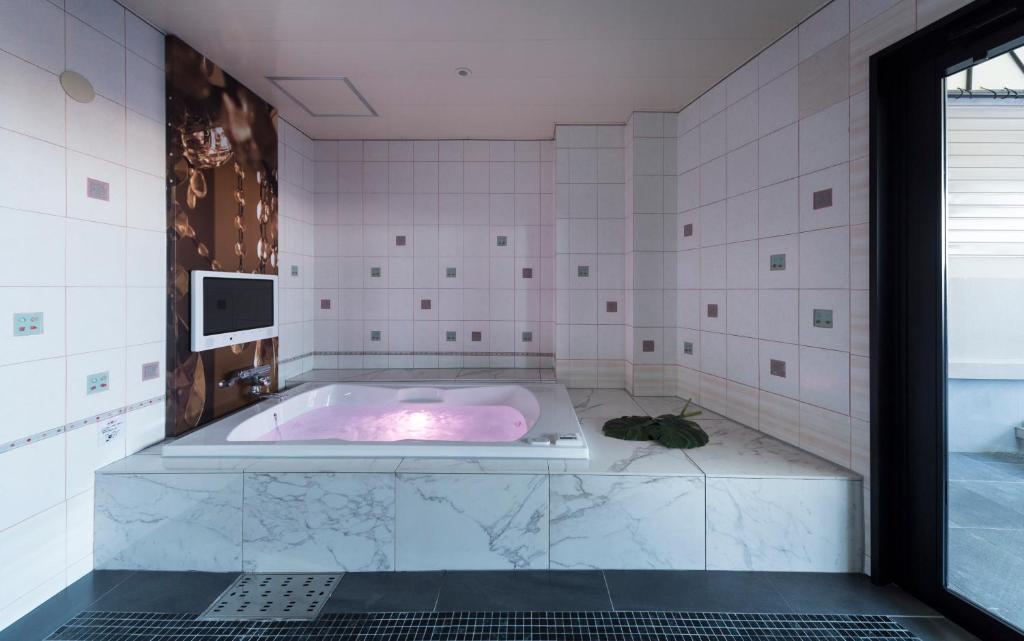 une baignoire rose dans une salle de bains carrelée de blanc dans l'établissement Hotel Plant Garden Resort (Adult Only), à Toyokawa