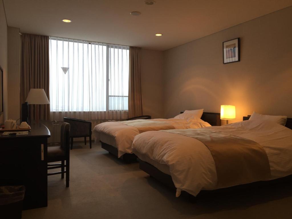 une chambre d'hôtel avec deux lits, un bureau et une fenêtre dans l'établissement Bekkan Yosanoso, à Miyazu