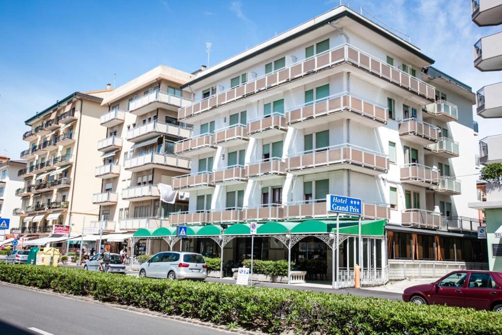 un grand bâtiment blanc avec des voitures garées devant dans l'établissement Hotel Grand Prix, à Sottomarina