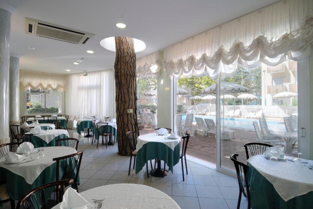 un restaurant avec des tables et des chaises et une grande fenêtre dans l'établissement Hotel Villa dei Fiori - sul mare con piscina, à Rimini