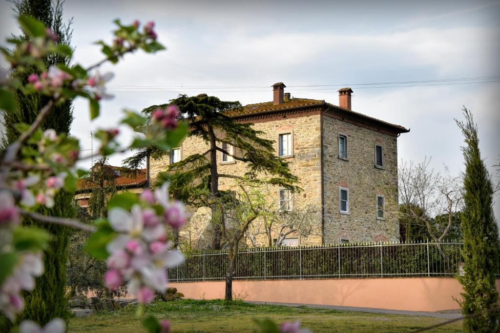 une ancienne maison en pierre avec une clôture et des fleurs roses dans l'établissement Villa Il Palazzo, à Cortone