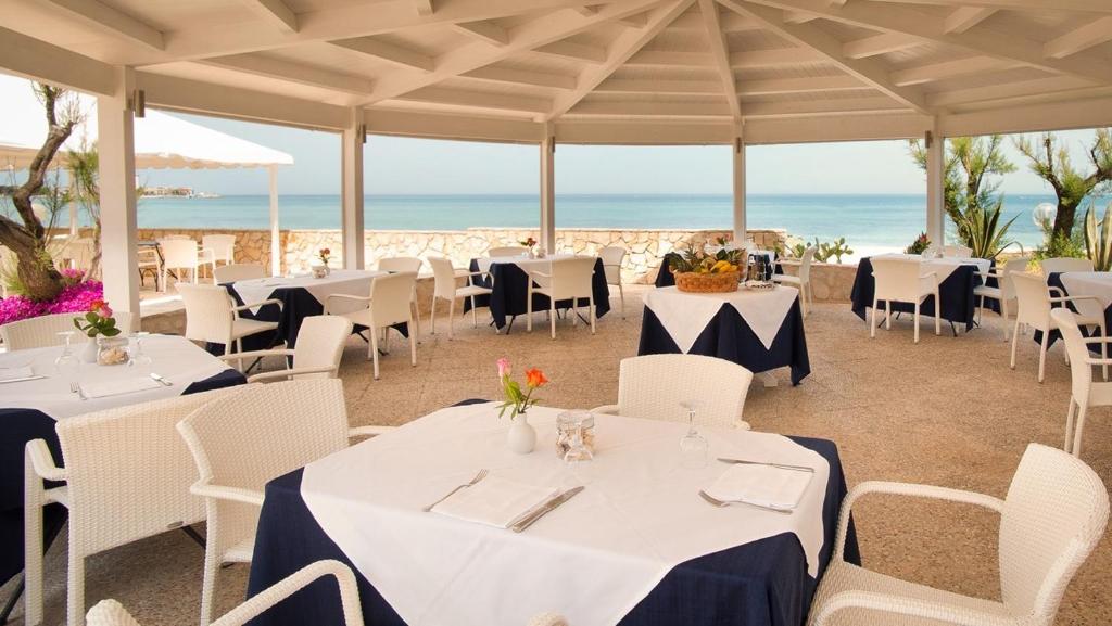 un restaurant avec des tables et des chaises blanches et l'océan dans l'établissement Hotel Del Levante, à Torre Canne
