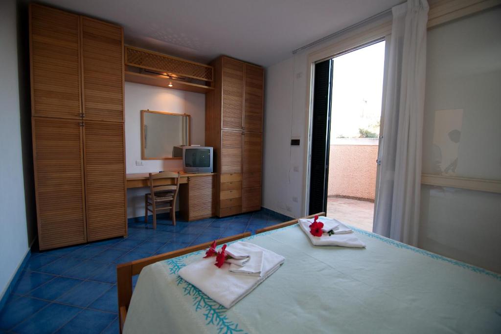une chambre avec un lit, un bureau et une télévision dans l'établissement Club Esse Roccaruja, à Stintino