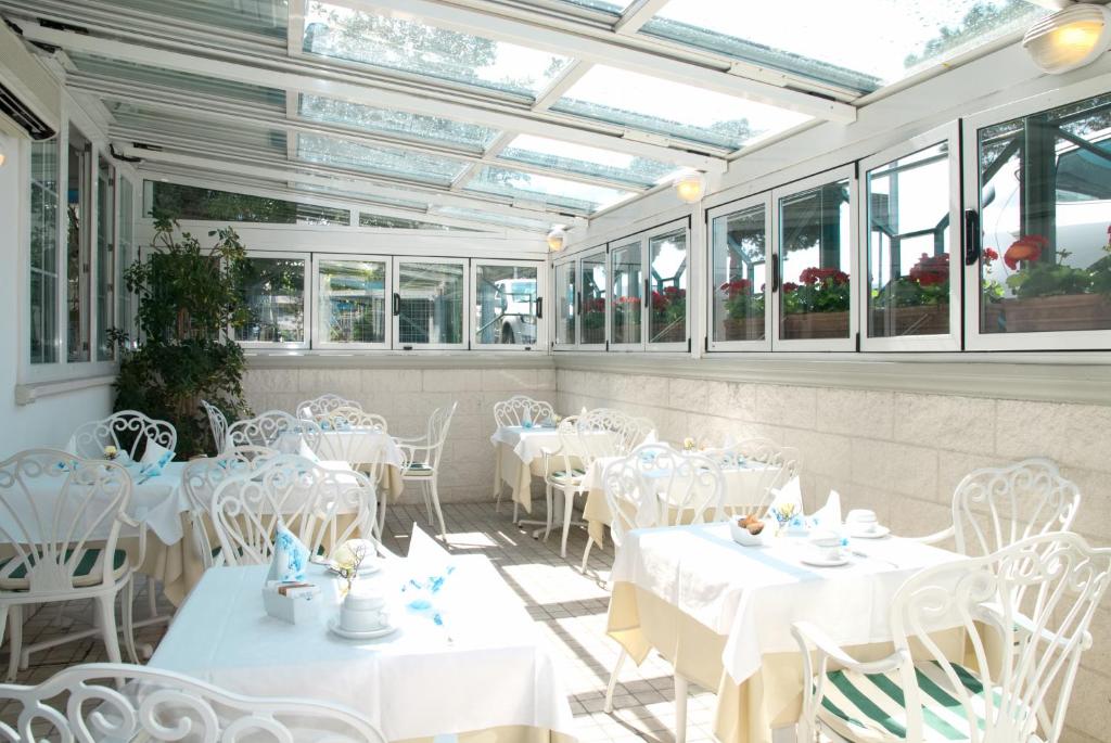 un restaurant avec des tables et des chaises blanches et des fenêtres dans l'établissement Hotel La Goletta, à Lignano Sabbiadoro