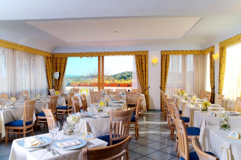 une salle à manger avec des tables et des chaises blanches et des fenêtres dans l'établissement Hotel Bellevue Benessere & Relax, à Ischia