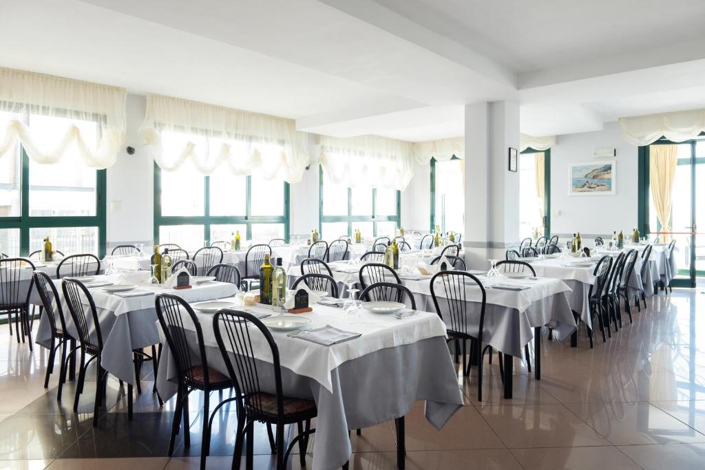 une salle de banquet avec des tables blanches, des chaises et des fenêtres dans l'établissement Hotel Emilia, à Rimini