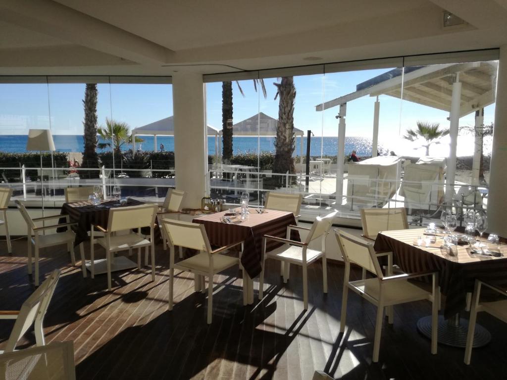 un restaurant avec des tables et des chaises avec l'océan en arrière-plan dans l'établissement Hotel De La Plage, à Pietra Ligure