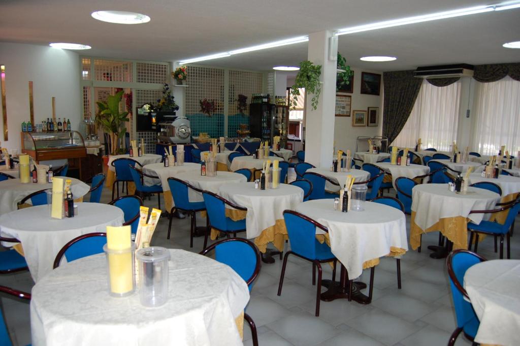 une salle à manger avec des tables blanches et des chaises bleues dans l'établissement Hotel Anfora, à Capoliveri