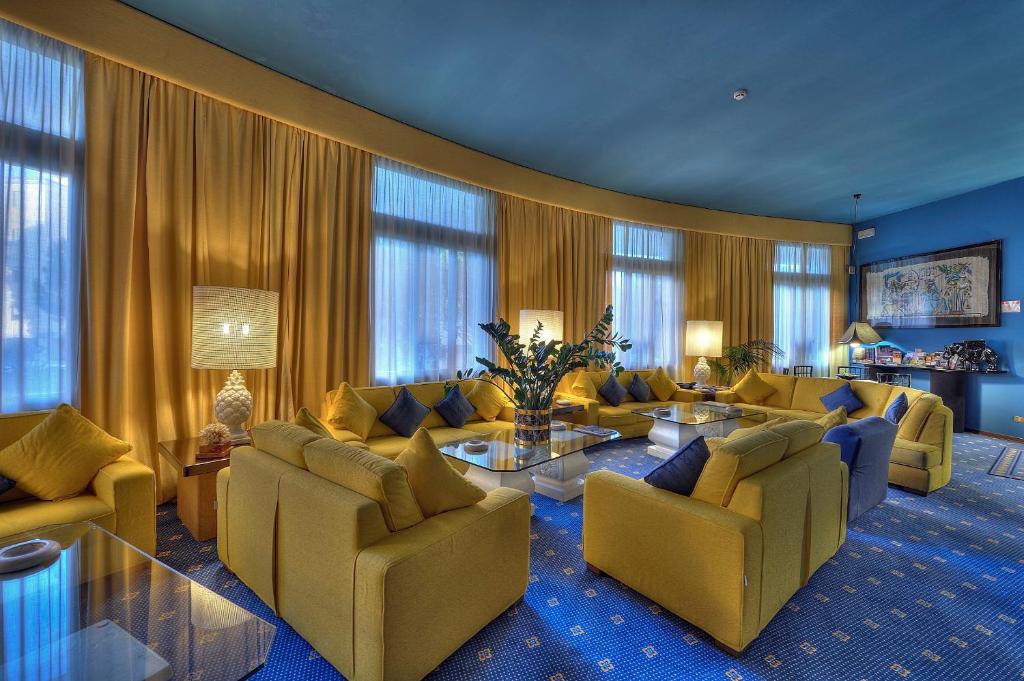 un salon avec des canapés, des tables et des fenêtres dans l'établissement Hotel Corallo, à Bibione