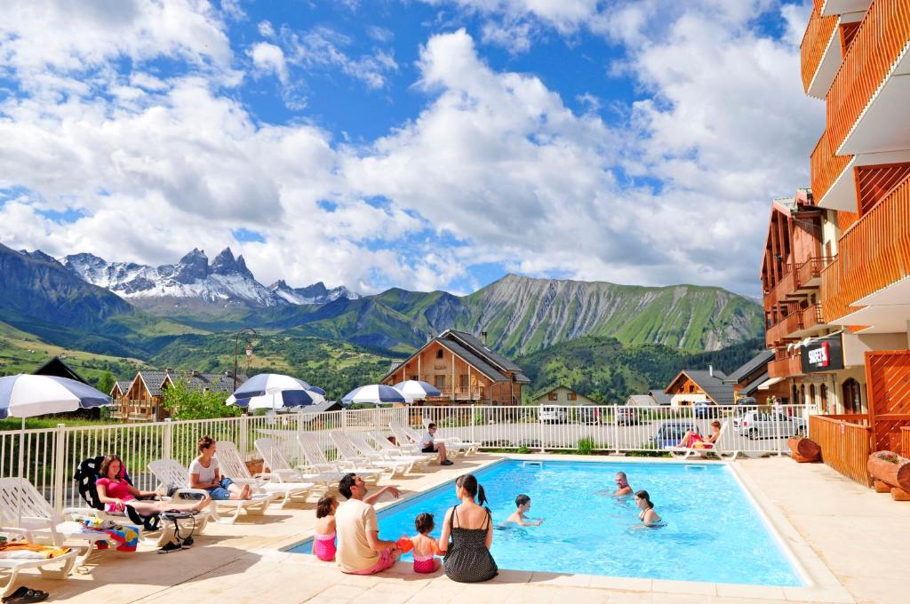 un groupe de personnes assises autour d'une piscine avec des montagnes dans l'établissement Résidence Goélia Le Relais des Pistes, à Albiez-le-Vieux