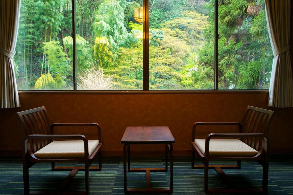 2 chaises et une table devant une grande fenêtre dans l'établissement Yugawara-Onsen Komachikan, à Yugawara