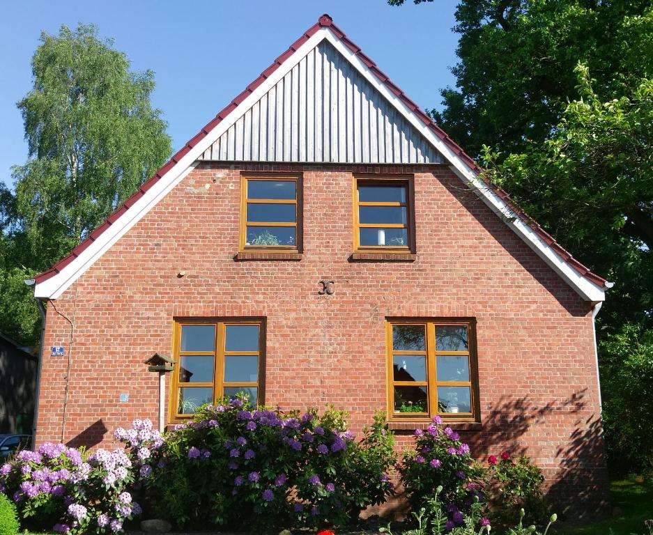 a red brick house with yellow windows and flowers at Hof Rahlf im Naturpark Aukrug in Hennstedt