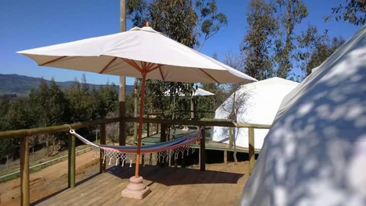 a hammock and an umbrella on a deck at Grado8punto8 Glamping Valle de Los Artistas in Lolol