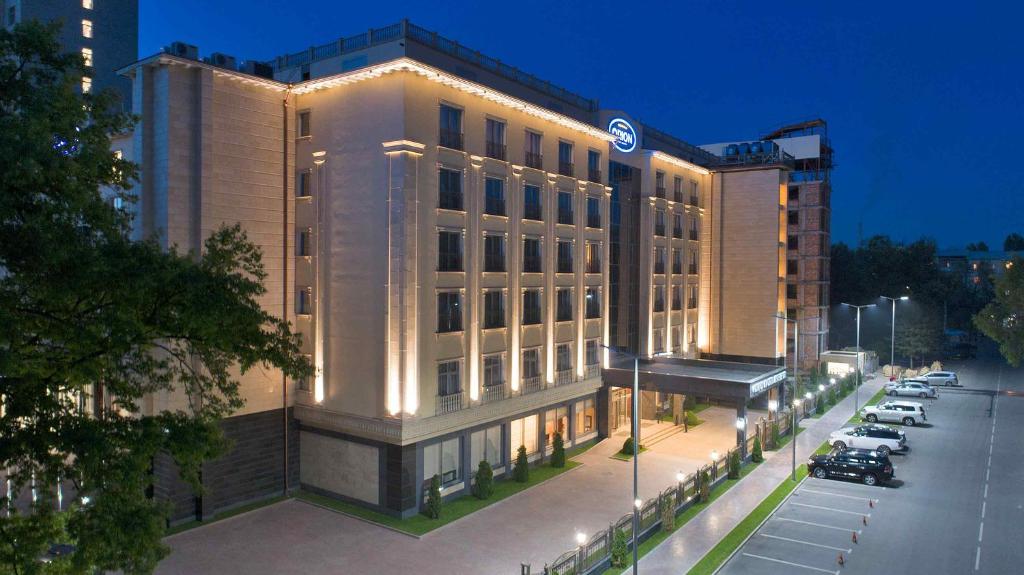 a lit up building with cars parked in a parking lot at Orion Hotel Bishkek in Bishkek