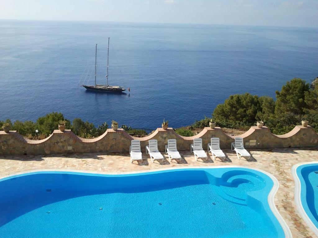 a swimming pool with chairs and a boat in the water at Hotel Diana in Ustica