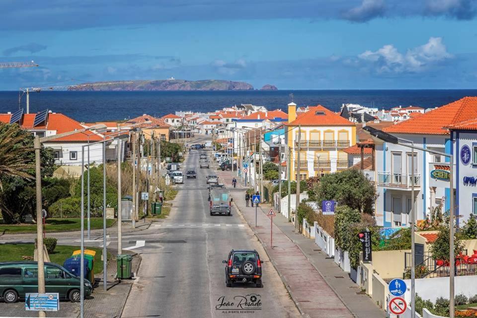 una calle de la ciudad con coches y casas y el océano en Baleal House en Peniche