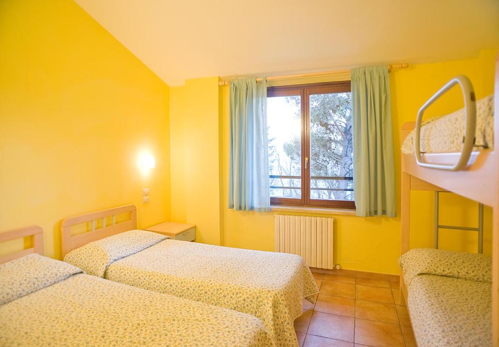 a yellow room with two beds and a window at Ostello Fontemaggio in Assisi