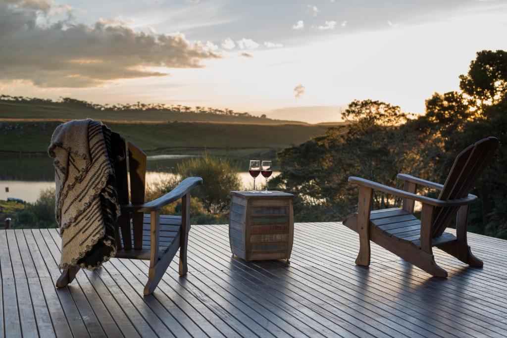 Duas cadeiras e uma mesa num deque com um copo de vinho em Rio do Rastro Eco Resort em Bom Jardim da Serra