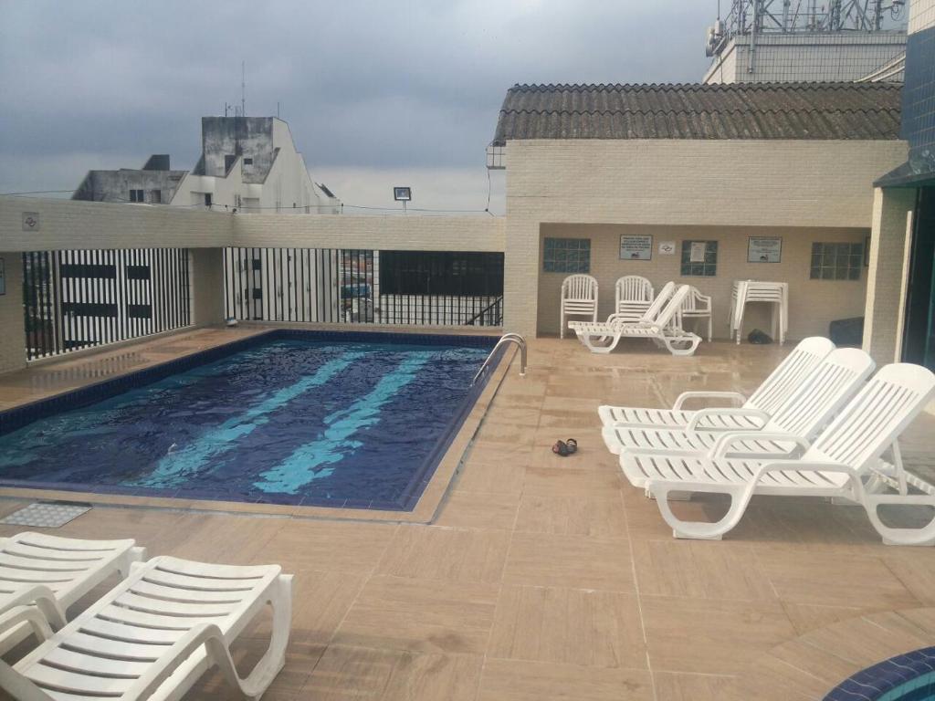 - une piscine avec des chaises blanches à côté d'un bâtiment dans l'établissement Flat Paladium, à São Vicente