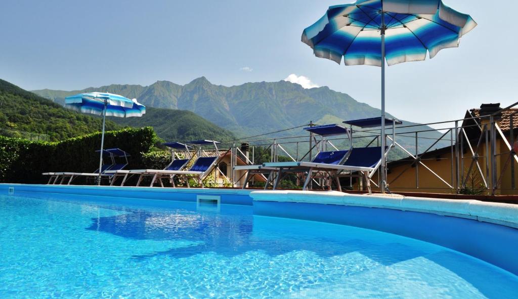 einen Pool mit Stühlen, Sonnenschirmen und Bergen in der Unterkunft Albergo Miramonti in Comano