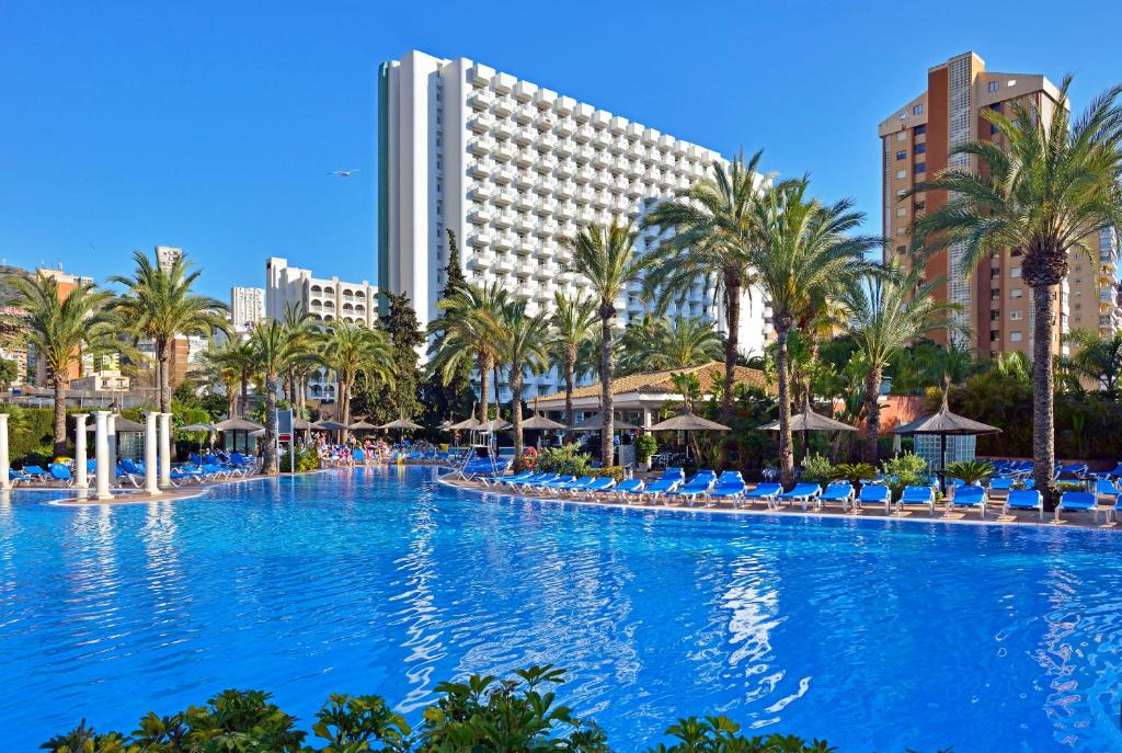 une grande piscine avec des palmiers et des bâtiments dans l'établissement Sol Pelicanos Ocas, à Benidorm