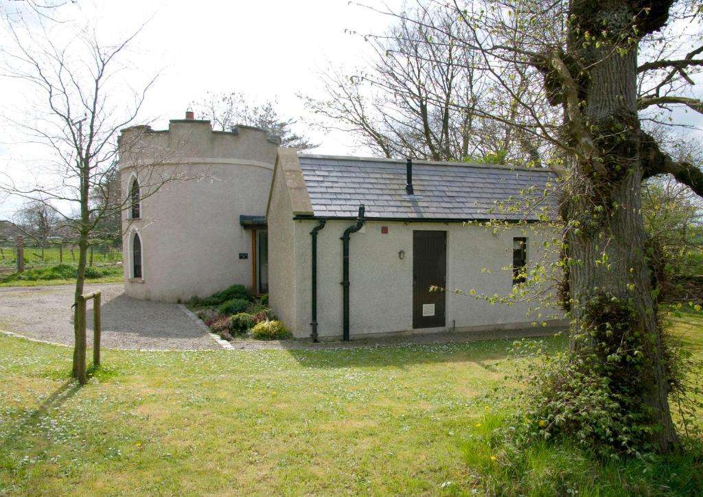 ein kleines weißes Gebäude mit einem Baum davor in der Unterkunft Drum Gate Lodge in Bushmills