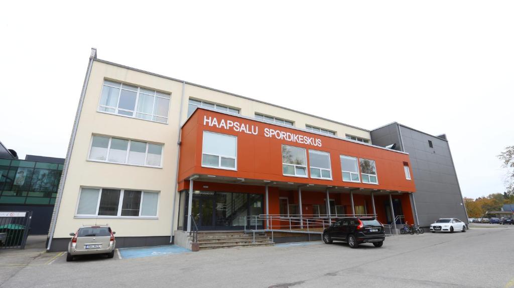 un bâtiment orange et blanc avec des voitures garées dans un parking dans l'établissement Sports Centre Haapsalu, à Haapsalu