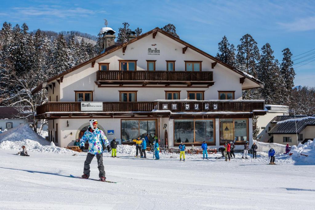 grupa osób jeżdżących na nartach przed domkiem narciarskim w obiekcie MARILLEN HOTEL by Hakuba Hotel Group w mieście Hakuba