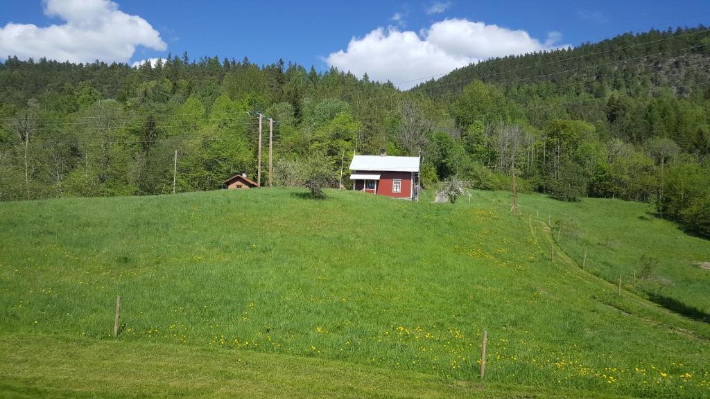 un pequeño edificio rojo en una colina con césped en Eidsfoss slusevokterbolig, en Lunde