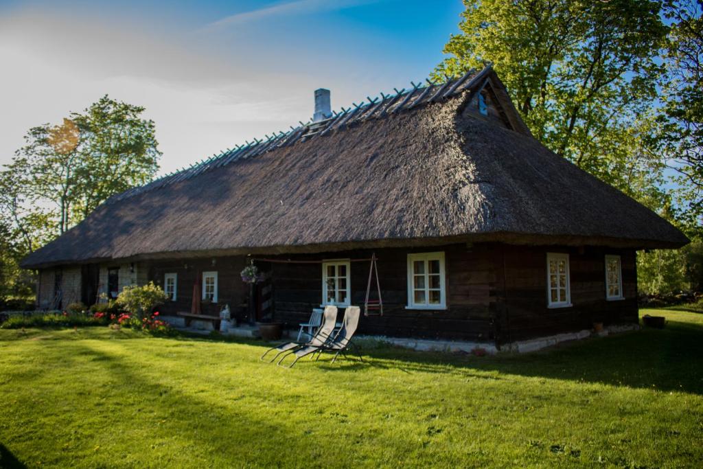 an old house with a thatched roof with two chairs at Kuusetuka Tourism Farm in Pähkla