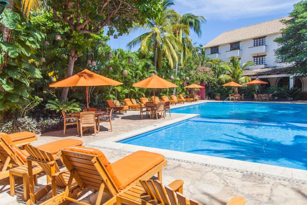 a pool with chairs and umbrellas next to a hotel at Villa Blanca Huatulco in Santa Cruz Huatulco