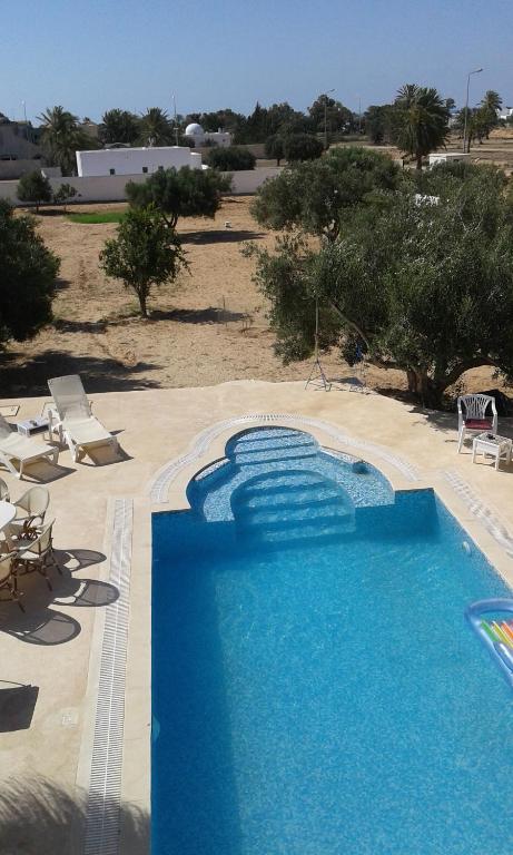 a large blue swimming pool with chairs and trees at Menzel Churasco Djerba in Aghīr