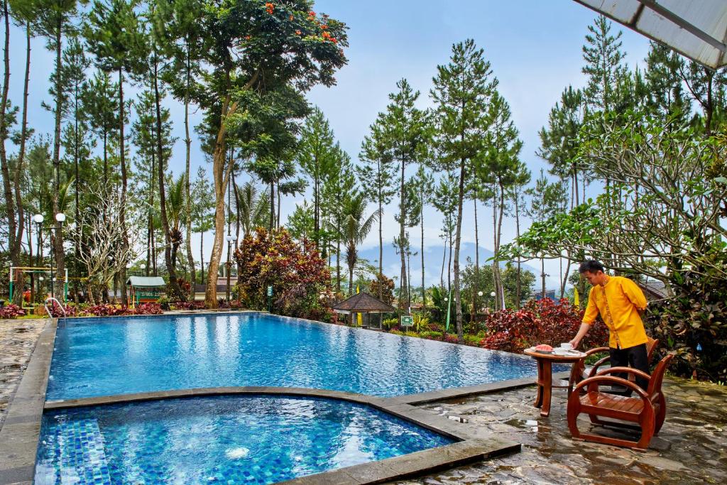 a man sitting on a chair next to a swimming pool at Jambuluwuk Convention Hall & Resort Puncak in Puncak