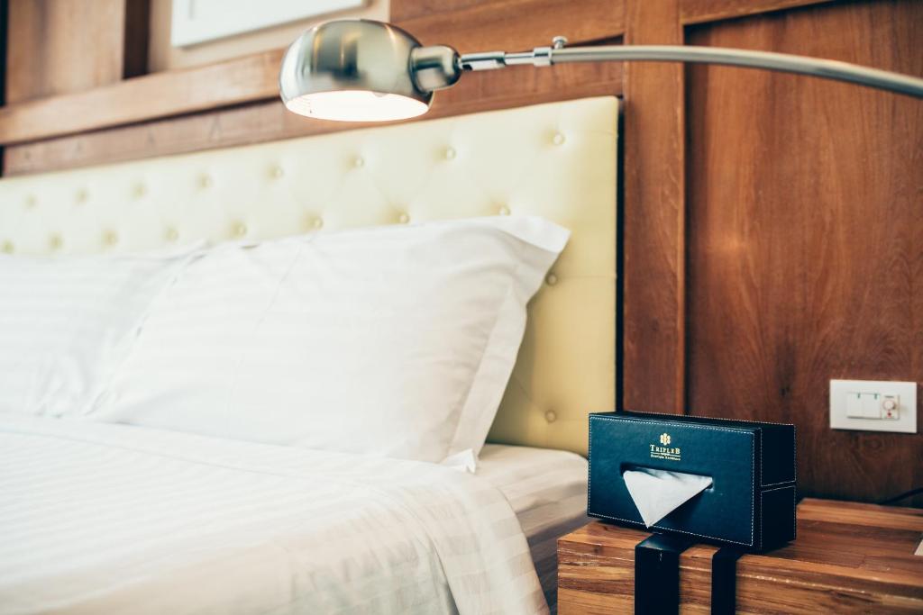 Dormitorio con cama con lámpara y libro en Triple B Boutique Residence, en Si Racha