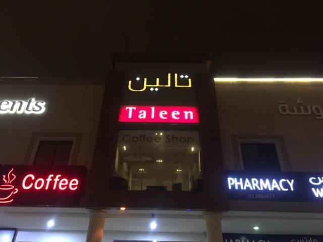 una tienda con letreros de neón al lado de un edificio en Taleen AlSahafa Hotel Apartments, en Riad
