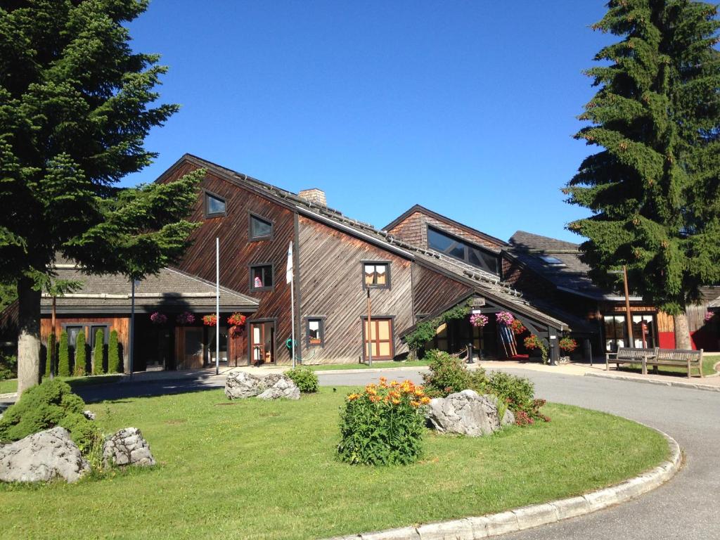 un grand bâtiment en bois avec des rochers dans l'herbe dans l'établissement Village Club Les Tavaillons, aux Carroz d'Arâches