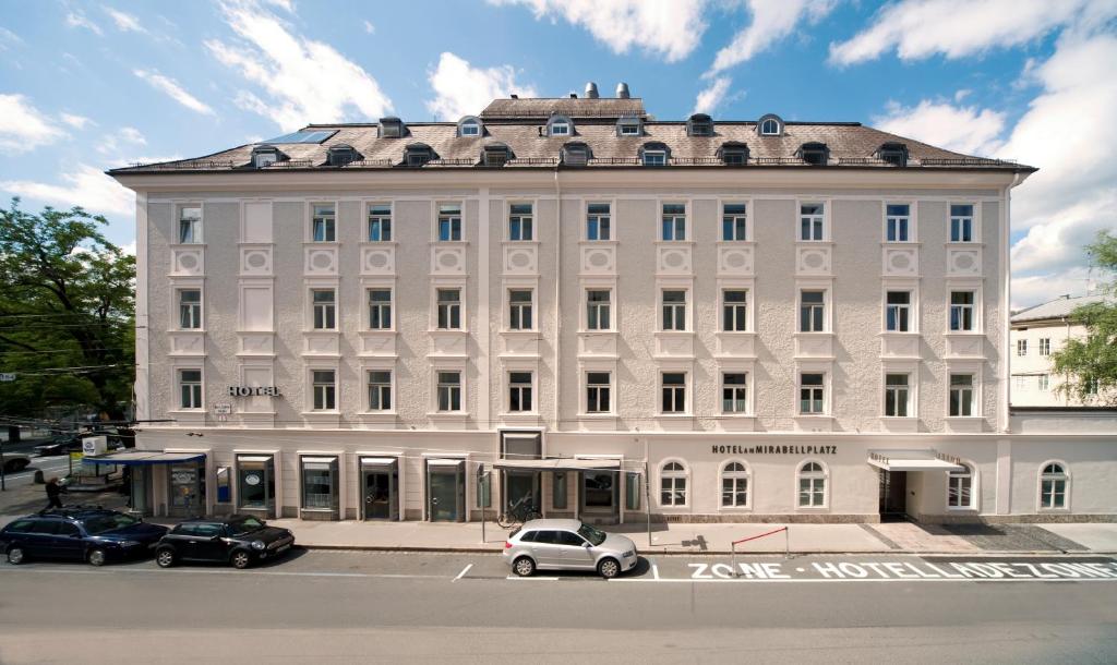 un edificio bianco con macchine parcheggiate di fronte di Hotel am Mirabellplatz a Salisburgo