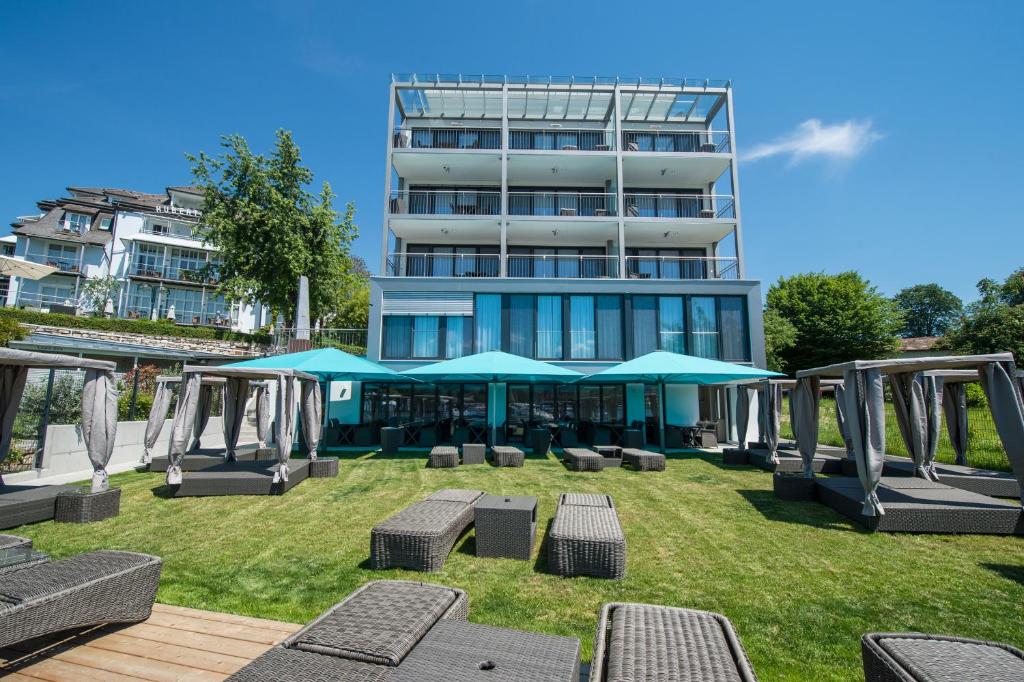 un bâtiment avec des chaises et des parasols dans l'herbe dans l'établissement Boutiquehotel Wörthersee - Serviced Apartments, à Velden am Wörther See