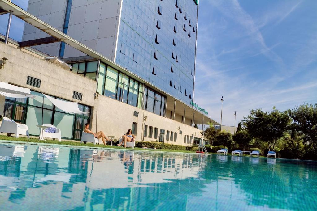 two people sitting in a swimming pool in front of a building at Oca Puerta del Camino Hotel in Santiago de Compostela