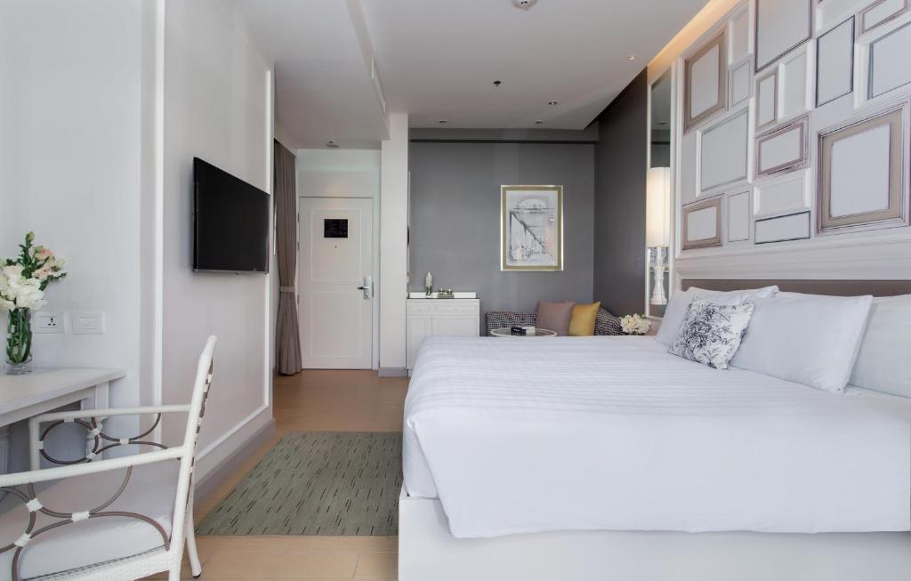 A bright bedroom pairs a large white bed with a compact desk and sitting area.