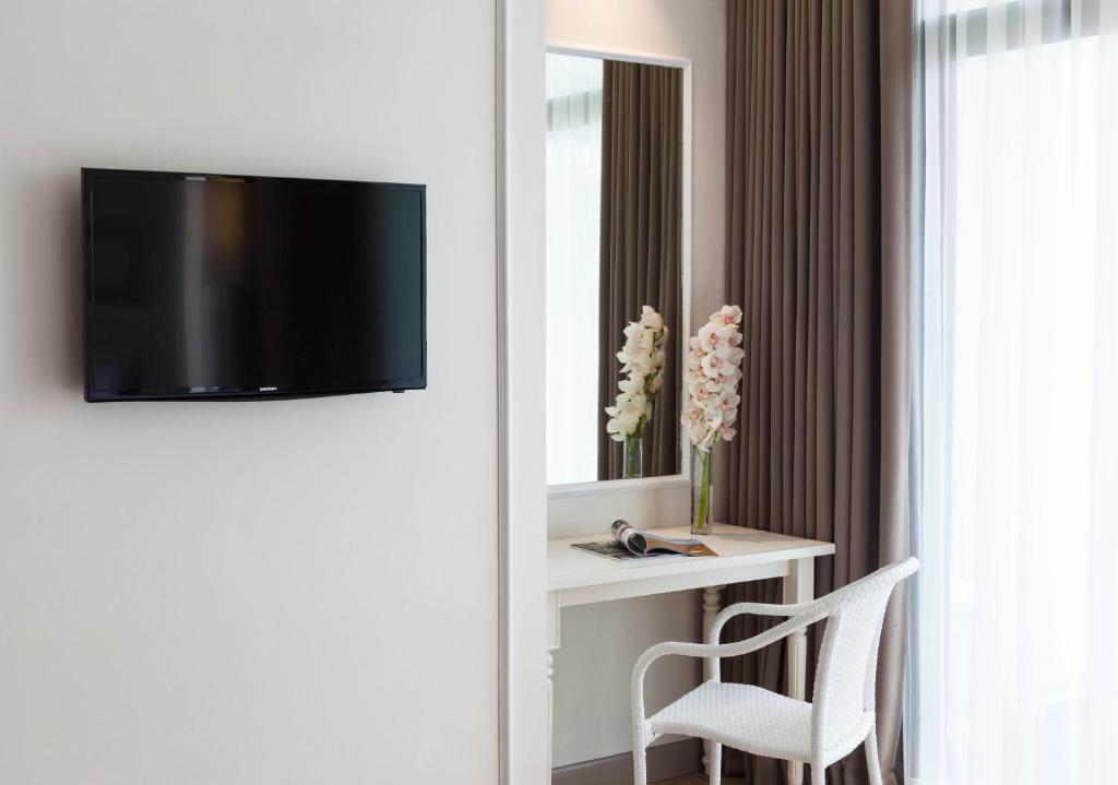 A compact in-room work corner sits beside a wall-mounted television and bright curtained window.