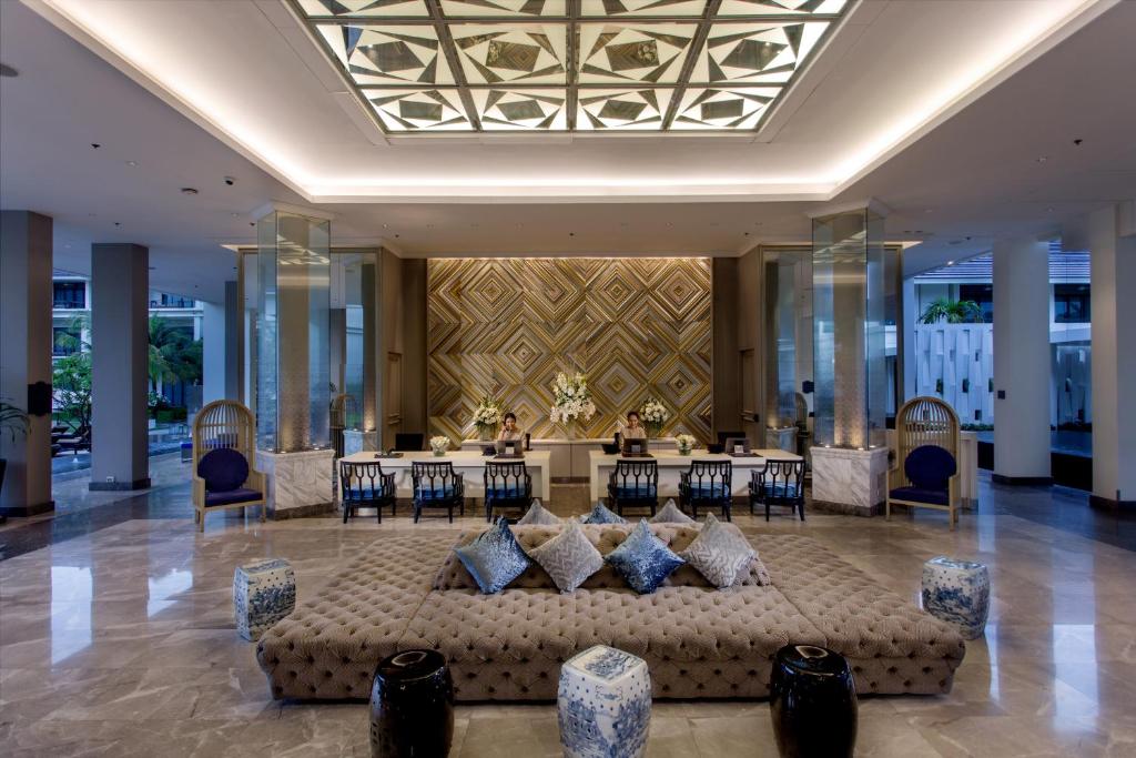 A grand hotel lobby with a central tufted sofa and patterned ceiling.