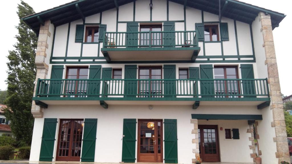 a house with green shutters and a balcony at Hotel Mendionde in Saint-Pée-sur-Nivelle