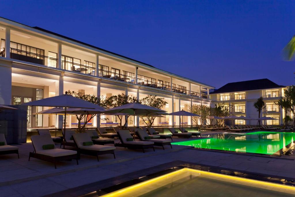 An illuminated pool courtyard is lined with loungers beneath a two-storey hotel wing.